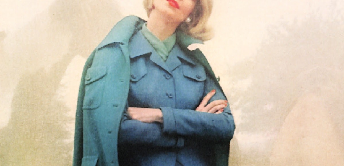 1950s woman wearing coat in peacock blue worn over a suit in a similar color.