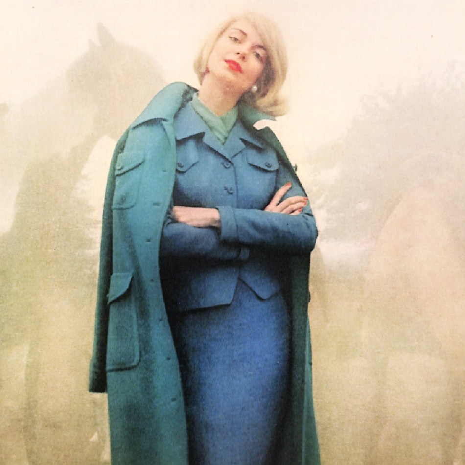 1950s woman wearing coat in peacock blue worn over a suit in a similar color.