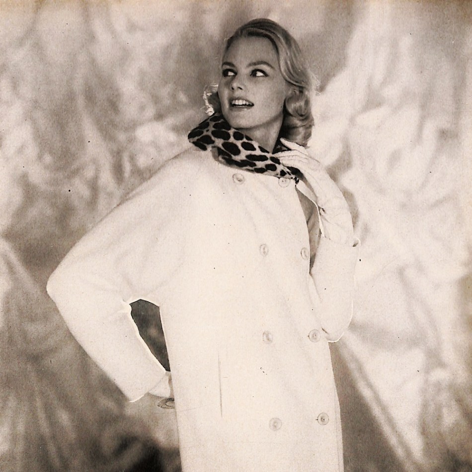 1950s woman wearing a white double-breasted coat with a leopard collar and white gloves.