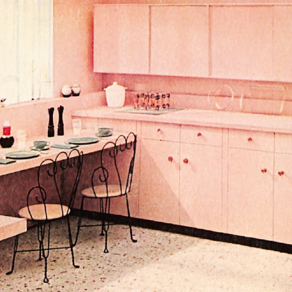 Vintage kitchen with pink walls, counters, cabinets, and floor. Also heart-shape black iron chairs.